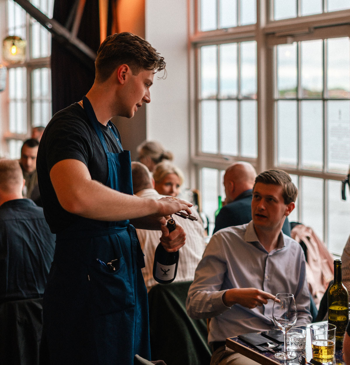 Tjener åbner vin ved et bord med gæster